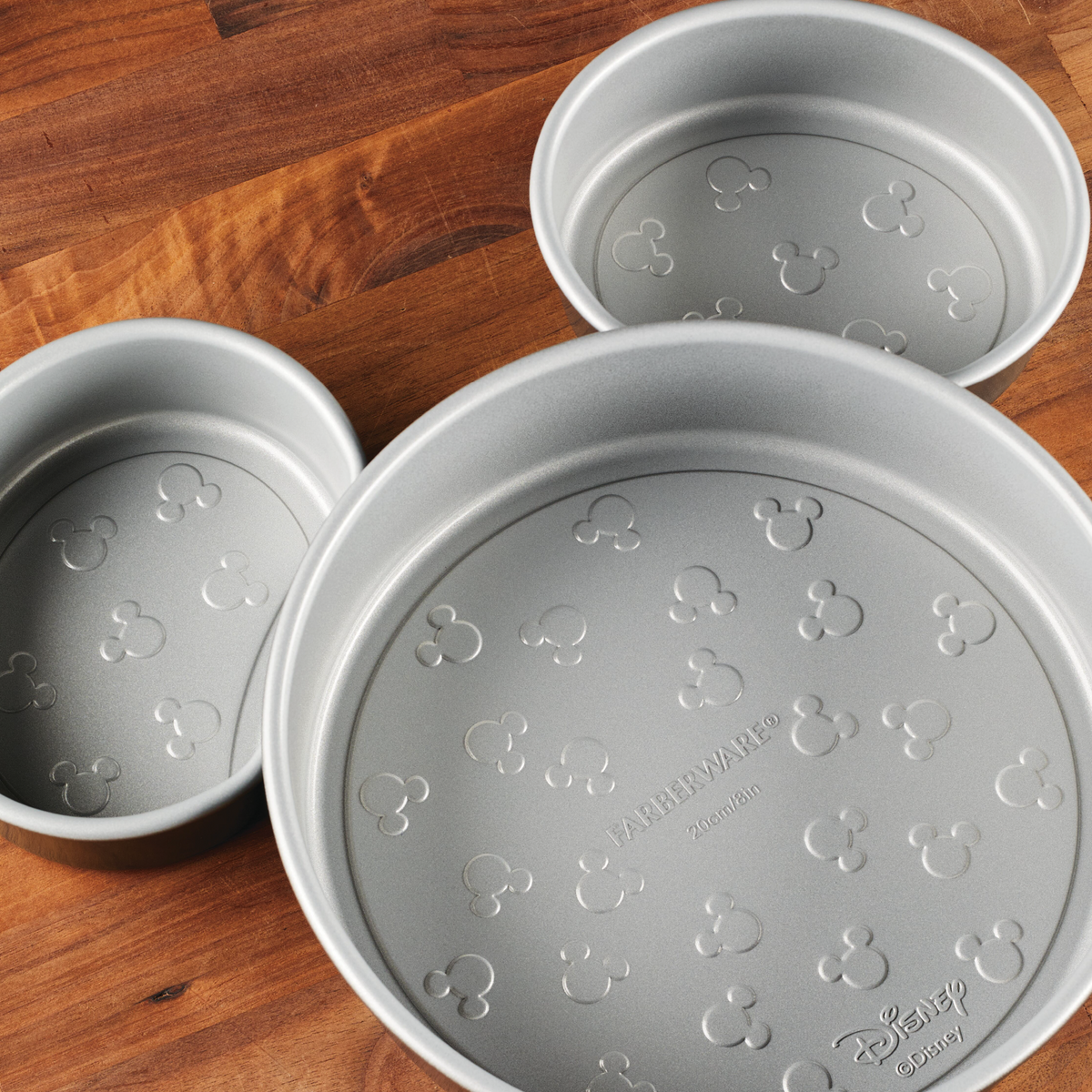 Three round baking pans with Mickey Mouse patterns on a wooden surface.
