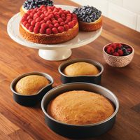 Cakes with fruit toppings and plain cakes, perfectly shaped thanks to the trusty 3-Piece Nonstick Mickey Head Cake Pan Set, sit invitingly on a wooden table.