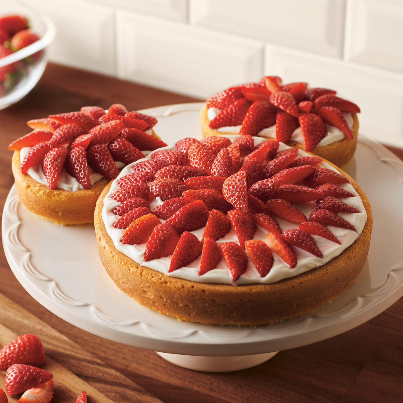 Three strawberry-topped cakes elegantly rest on a white cake stand, showcasing the magic of your favorite 3-Piece Nonstick Mickey Head Cake Pan Set.