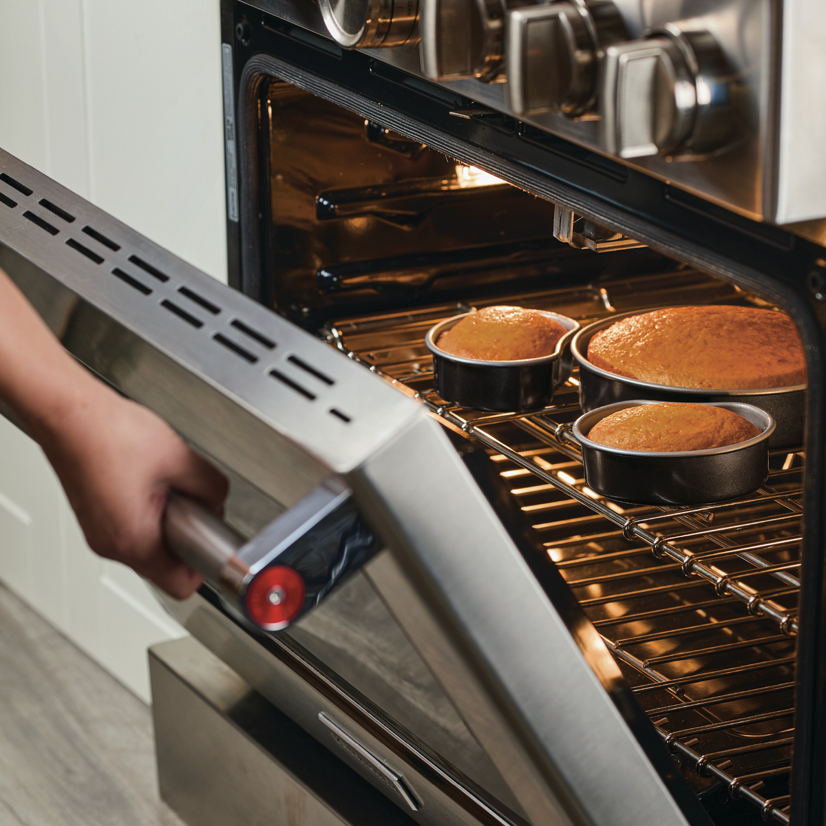 Person checking cakes baking in an open oven.