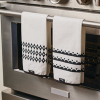 Two stylish Disney "Home Monochrome" kitchen towels, featuring Mickey Mouse-inspired black patterns, are draped elegantly over an oven handle.
