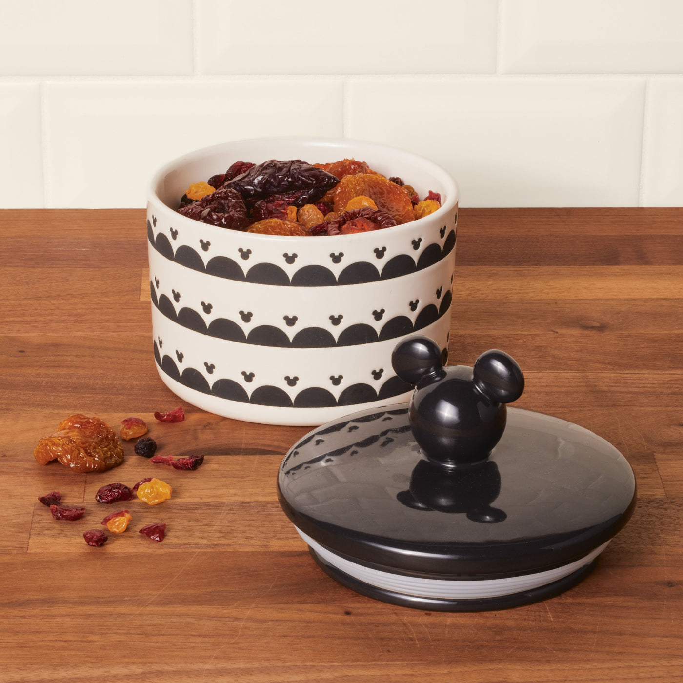 A Ceramic Jar with Airtight Lid, embellished with stripes, rests on a wooden countertop, keeping the assortment of dried fruits securely sealed inside.