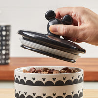 A hand lifting the airtight lid from the Ceramic Jar with Airtight Lid, which is filled with nuts.