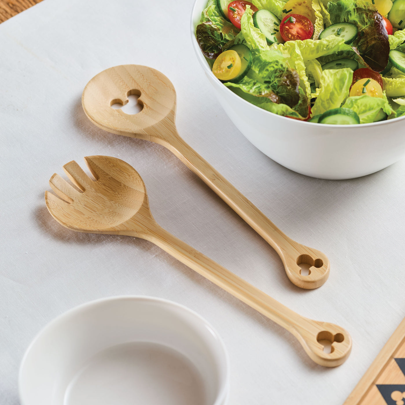 A salad, elegantly showcased with a 2-Piece Bamboo Salad Server Set, rests gracefully on a white tablecloth.