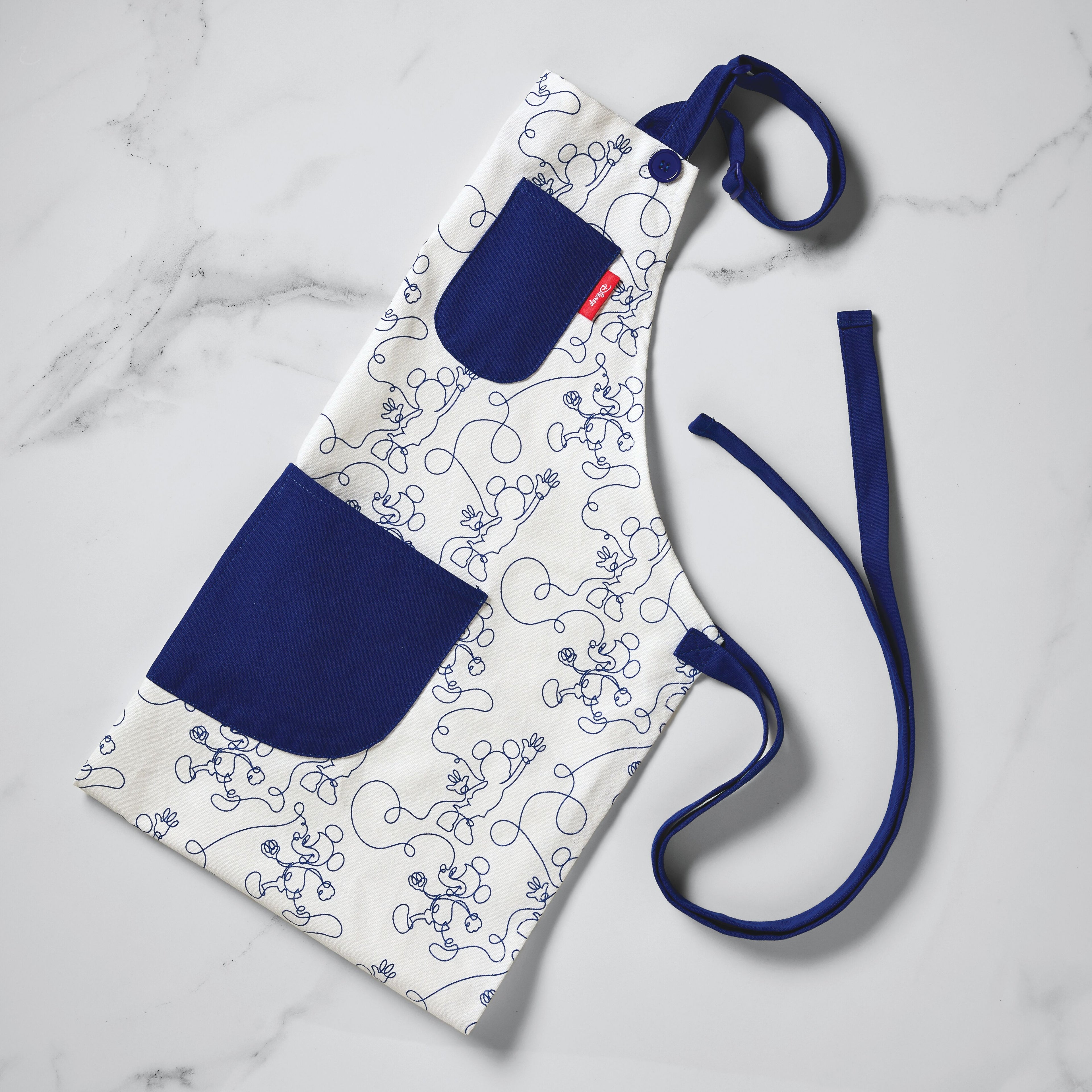 Bon Voyage Apron featuring a white base with a blue pocket adorned with an abstract line drawing design, ideal for Disney Home enthusiasts.