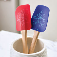 The Bon Voyage 2-Piece Spatula and Spoonula Set, adorned with a charming Disney Mickey Mouse design in red and blue, rests in a white holder on the kitchen counter.