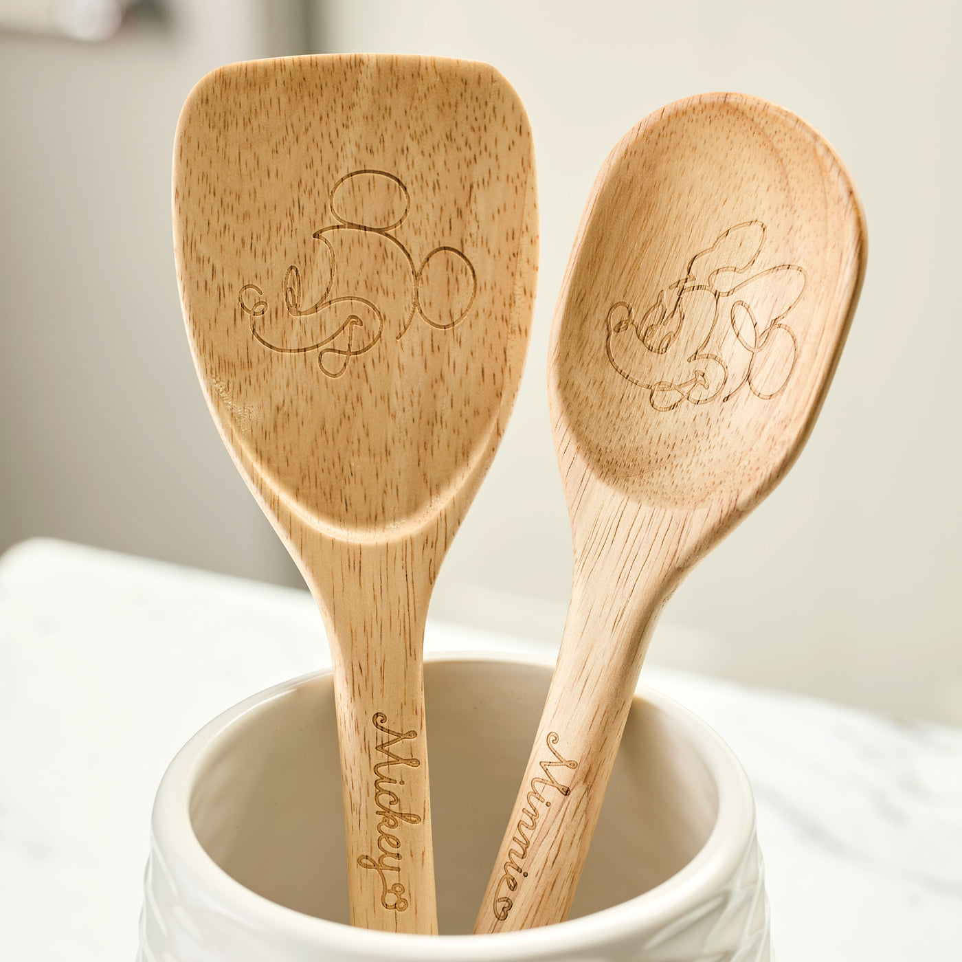 The Bon Voyage 2-Piece Spoon and Turner Set from the Disney Home collection features two wooden cooking spoons engraved with designs of beloved cartoon characters, including Mickey Mouse.