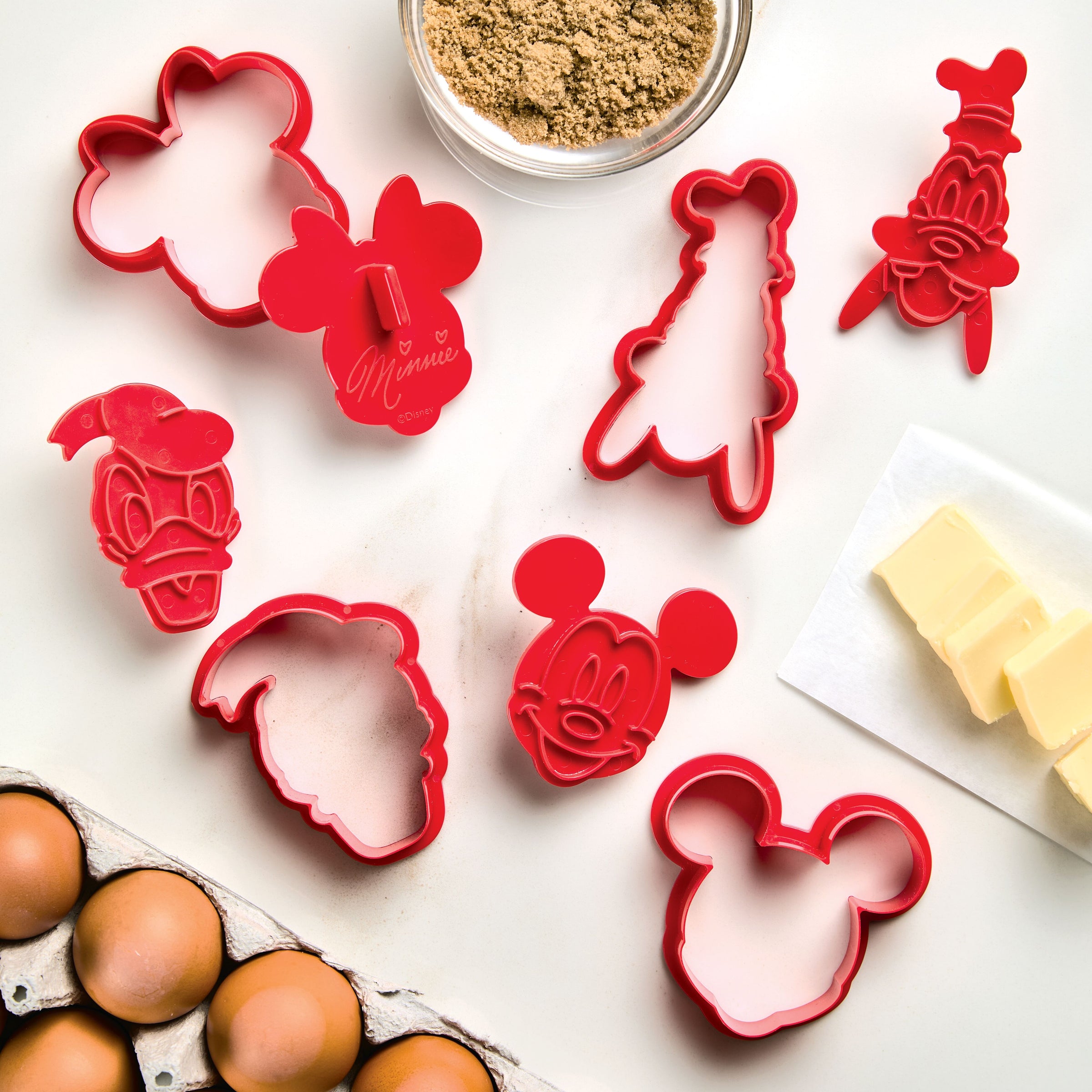On the counter, a Bake with Mickey Mouse 8-Piece Cookie Cutter and Stamp Set waits alongside eggs and butter, perfect for making treats with Mickey and Friends.