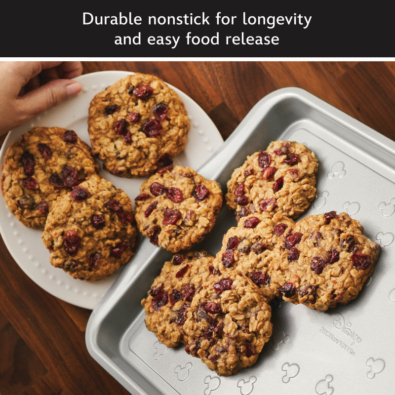 A hand places cranberry oatmeal cookies on a plate with a 6-Piece Bakeware Set.