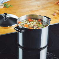 The Classic Series Stainless Steel Stockpot With Lid simmers a batch of vegetable soup on the stovetop, highlighting its durability and long-lasting performance.