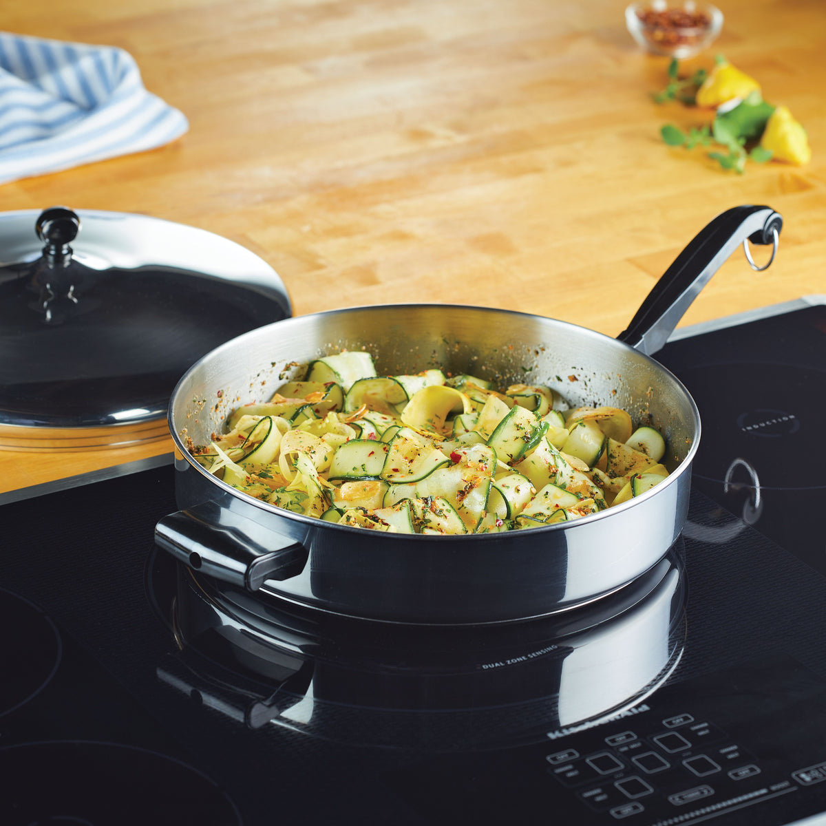 A frying pan on a stove with cooked zucchini ribbons and spices.