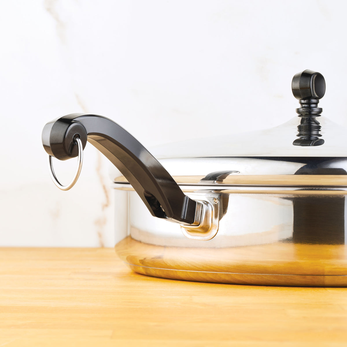 Close-up of a lidded stainless steel pot with a black handle on a wooden surface.
