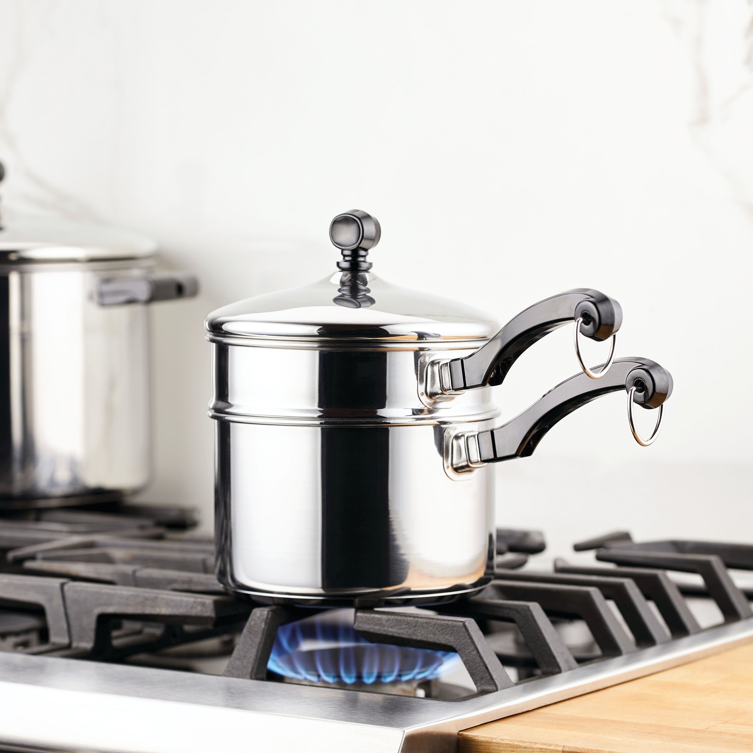 A Classic Series Stainless Steel 2-Qt. Covered Saucepan with a self-basting lid elegantly sits on the lit gas stove burner.