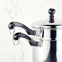 A stacked stainless steel saucepan with black handles featuring a matching self-basting lid, part of the Classic Series 2-Qt. Covered Saucepan with Double Boiler Insert.