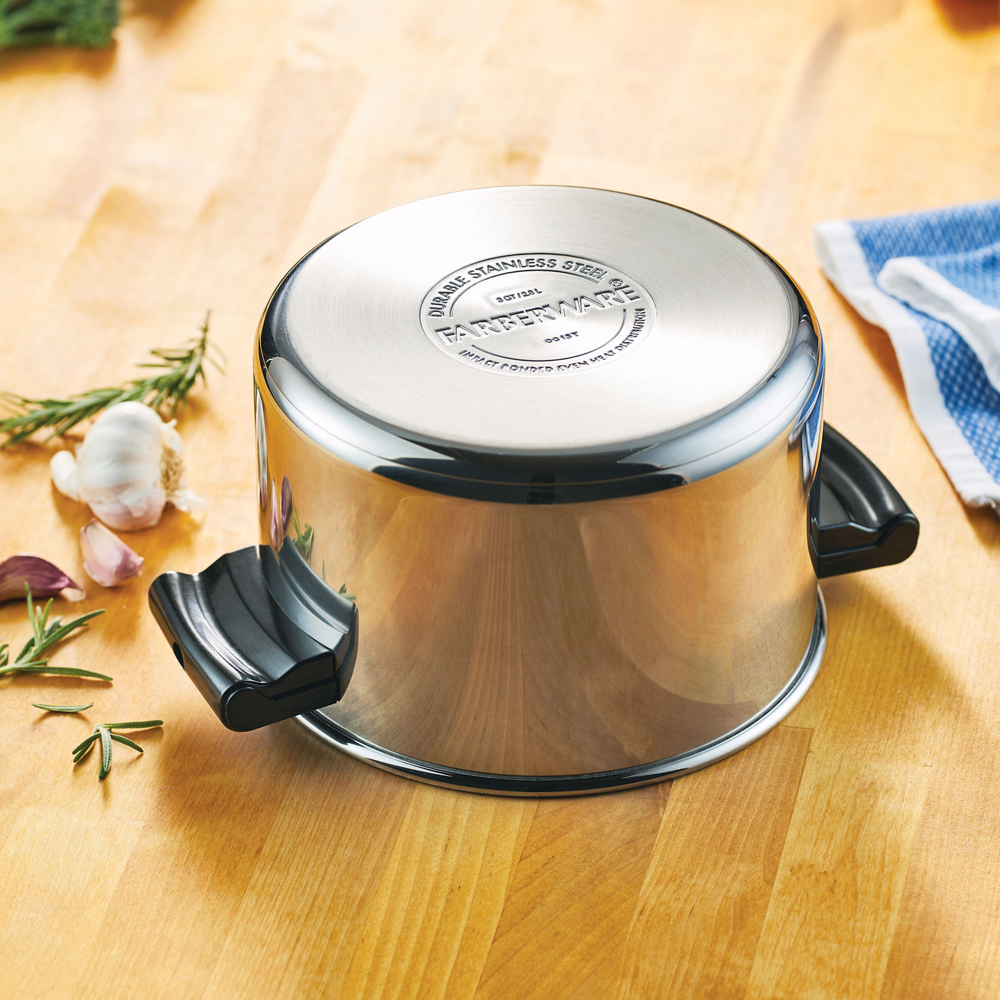 The Classic Series Stainless Steel 3-Qt. Saucepot with Steamer Insert is positioned upside down on a wooden surface, surrounded by various kitchen items.