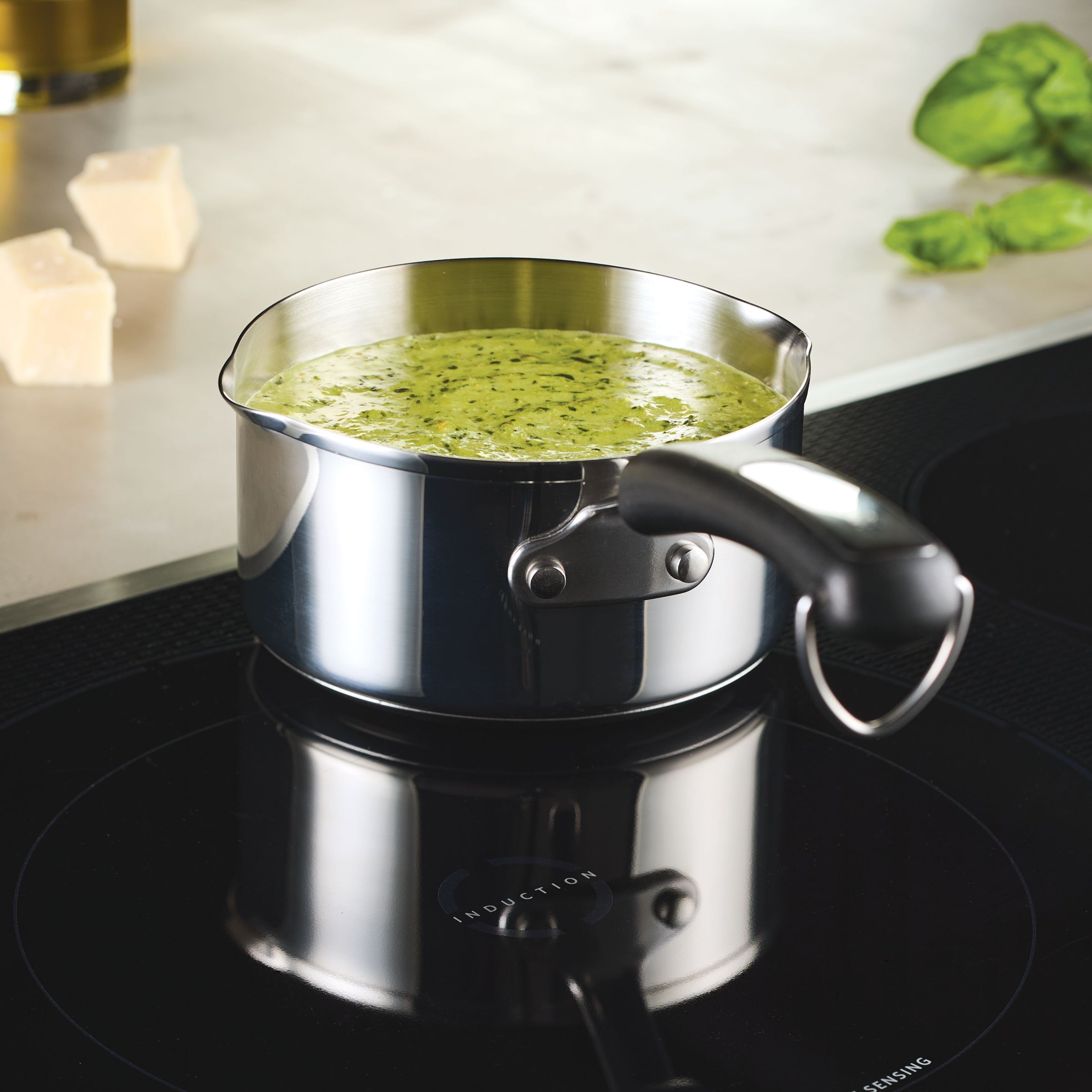 The 1-Quart Stainless Steel Saucepan filled with green sauce simmers on the induction cooktop, perfect for everyday cooking.