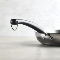 Close-up of a black pan handle on a gray background, highlighting the sleek design of the 12.25-Inch Stainless Steel Frying Pan from Farberware Brilliance cookware.