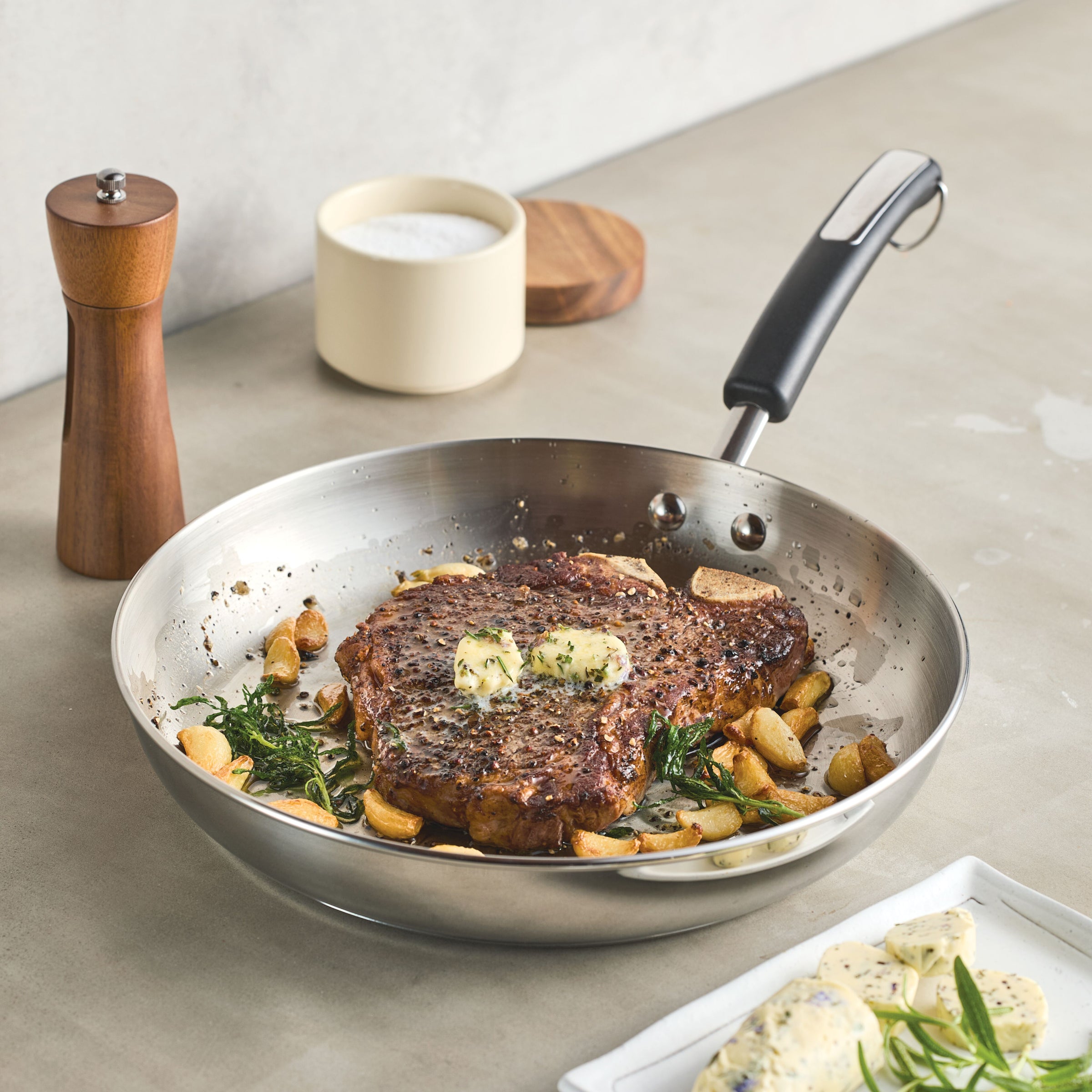 A steak infused with garlic and herbs sizzles in a frying pan, enveloped by spices and cooked to perfection using the reliable 12.25-Inch Stainless Steel Frying Pan from Farberware Brilliance.