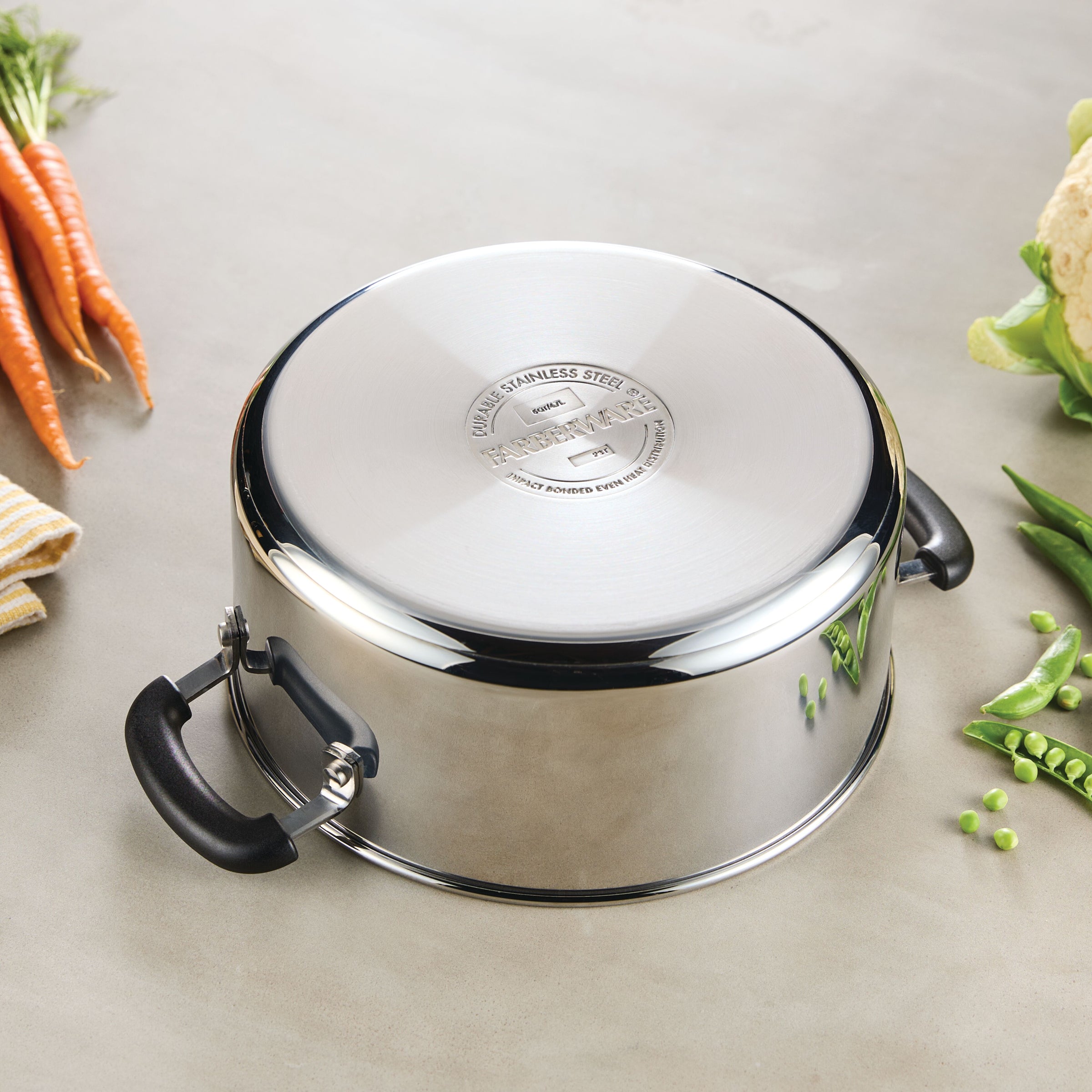 The 5-Quart Stainless Steel Dutch Oven sits upside-down on the counter, surrounded by colorful vegetables—an essential piece for everyday cooking.