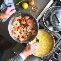 A person uses a 10 Inch Steamer Insert Stainless Steel to cook shrimp over pasta.