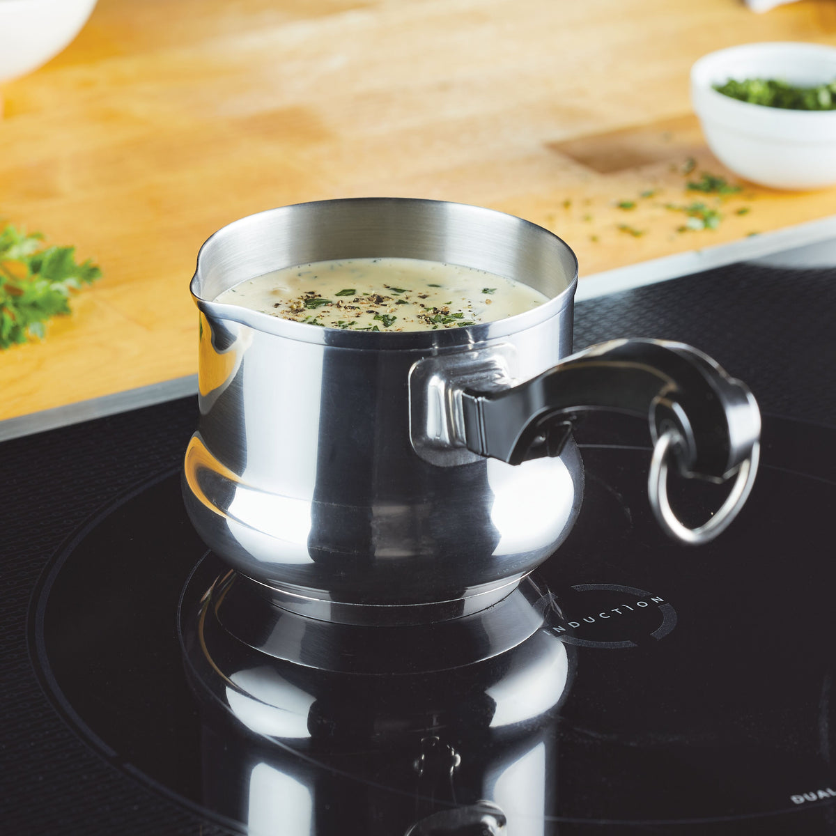 Metal pot with creamy soup on induction stove, herbs nearby.