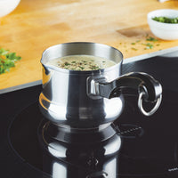 Metal pot with creamy soup on induction stove, herbs nearby.