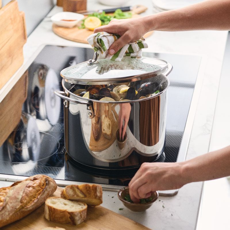 Person lifts lid off Stainless Steel 8-Quart Stockpot of mussels on stove.