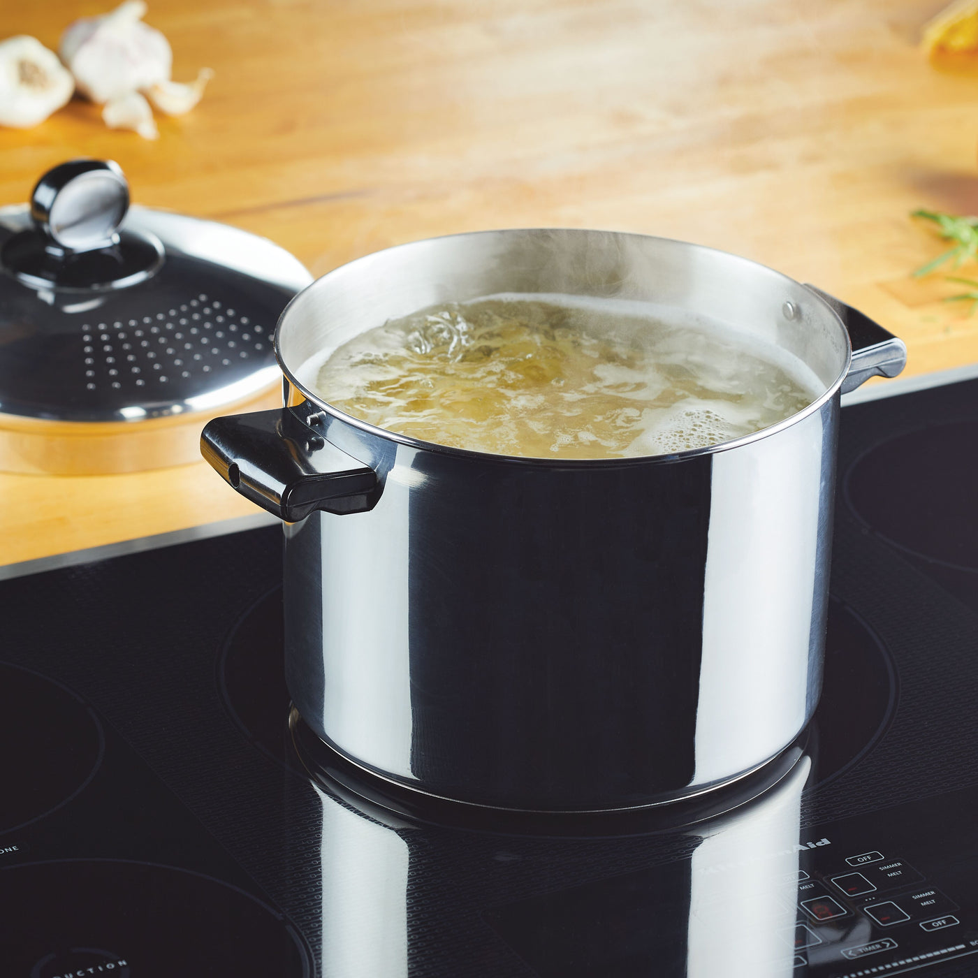 An 8-Quart Stockpot with a straining lid rests on the induction stove, its lid clattering gently as water boils beneath. Ideal for big batch cooking, this kitchen essential ensures efficiency and durability in every culinary endeavor.