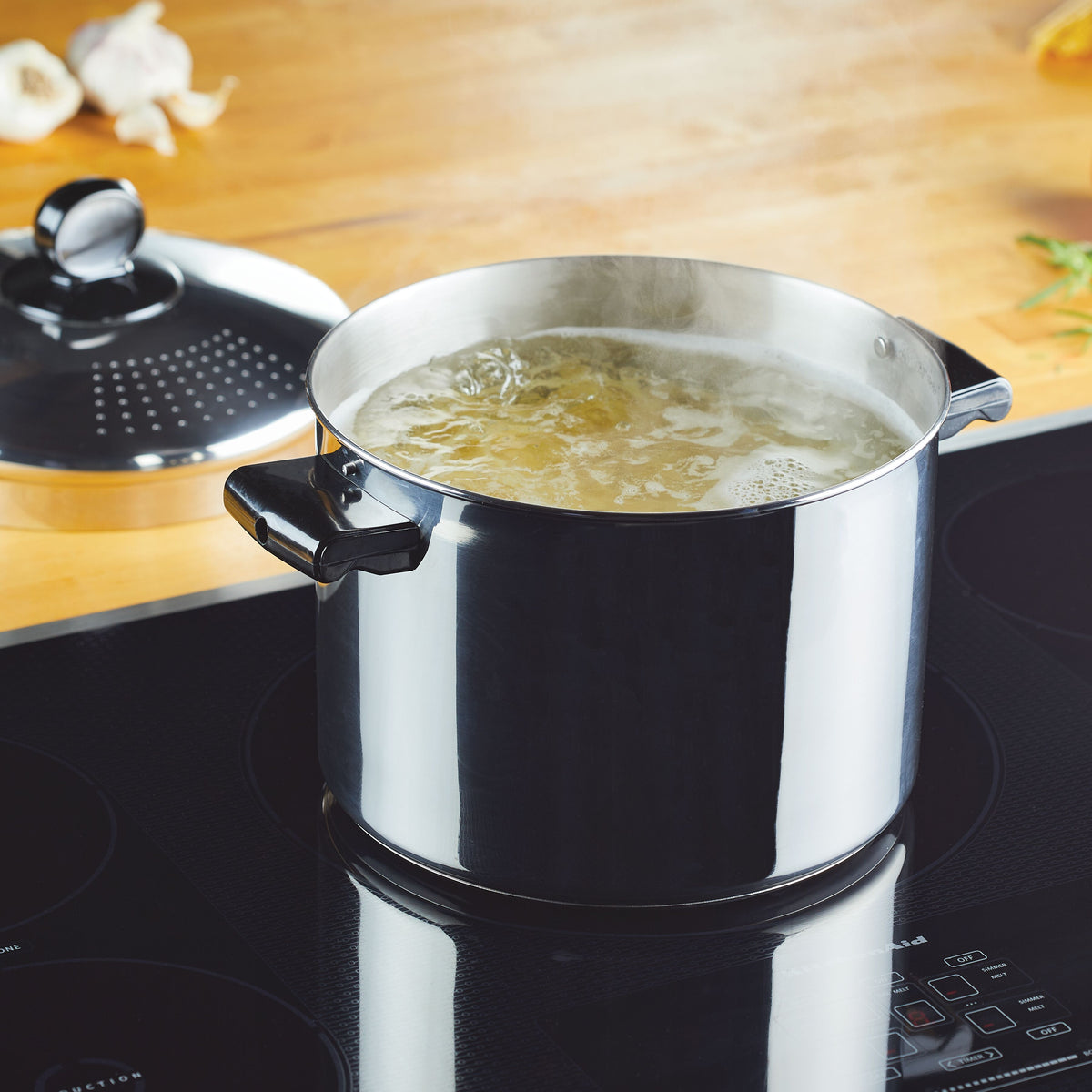 A pot of water boiling on an induction cooktop with a lid nearby.