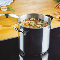 A large Classic Series Stainless Steel 11-Qt. Stockpot is filled with vegetable soup and pasta on the stovetop, with its lid neatly placed beside it. Known for its durability, this stockpot guarantees long-lasting performance for every hearty meal you prepare.
