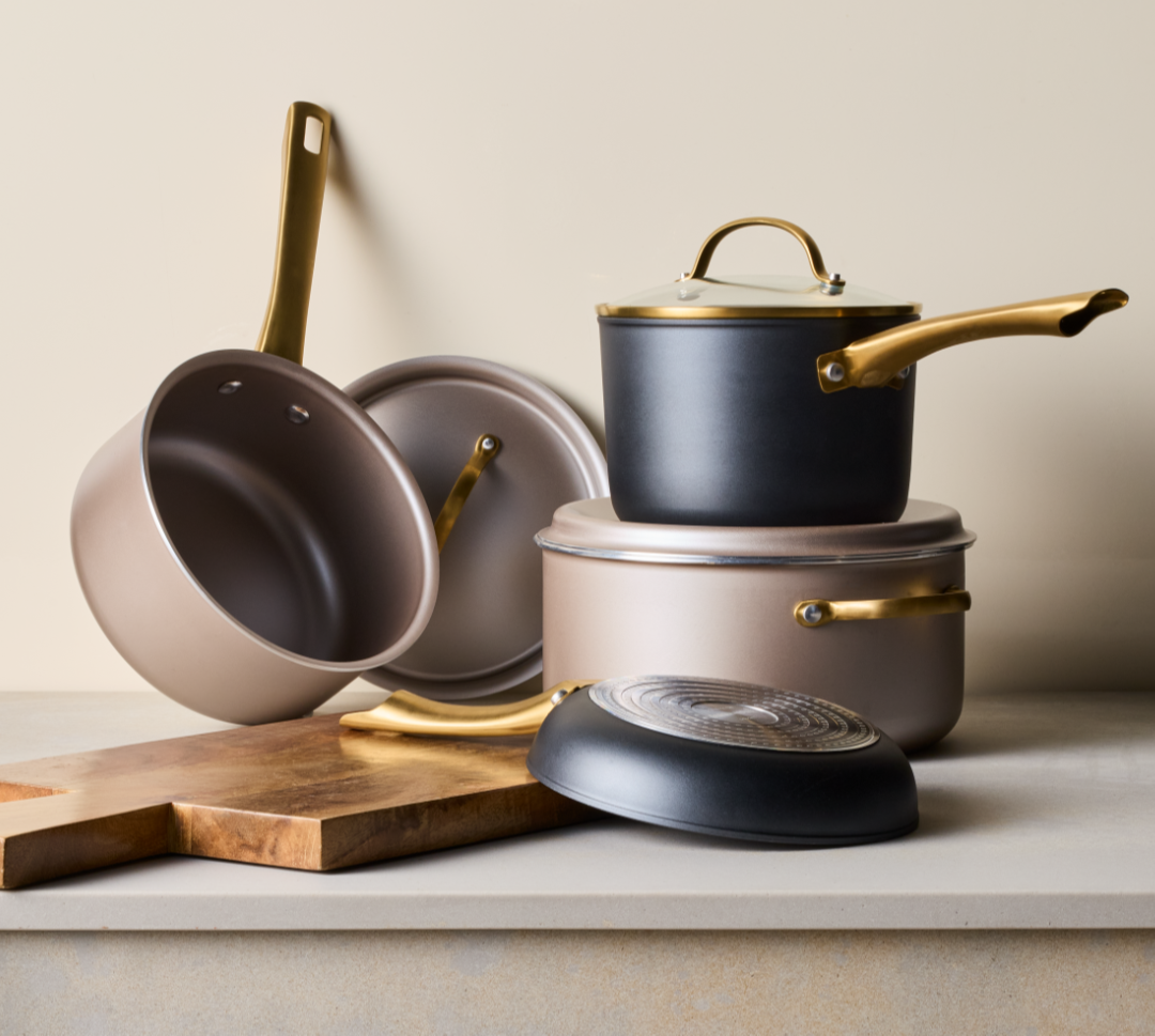 Radiant and Forged Induction Cookware stacked next to a wooden cutting board