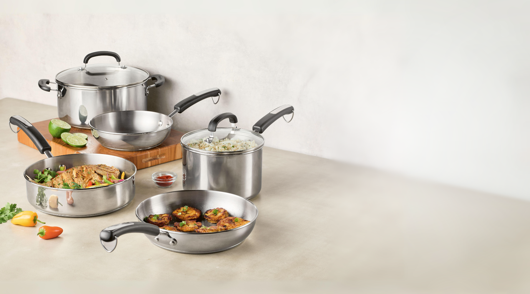 A set of stainless steel cookware with food displayed on a kitchen surface.