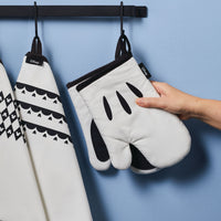 A hand holds an oven mitt from the Monochrome 5-Piece Set against a blue wall, adding a touch of Disney Home charm to your kitchen set.
