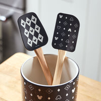 The Monochrome Kitchen Tool Set includes two patterned black-and-white bamboo silicone spatulas, elegantly displayed in a decorated black container, adding a touch of charm to your Disney kitchen tools collection.