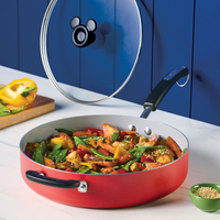 Red pan with stir-fried chicken and vegetables on a marble counter.