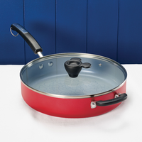 Red frying pan with a glass lid on a white surface against a blue background.