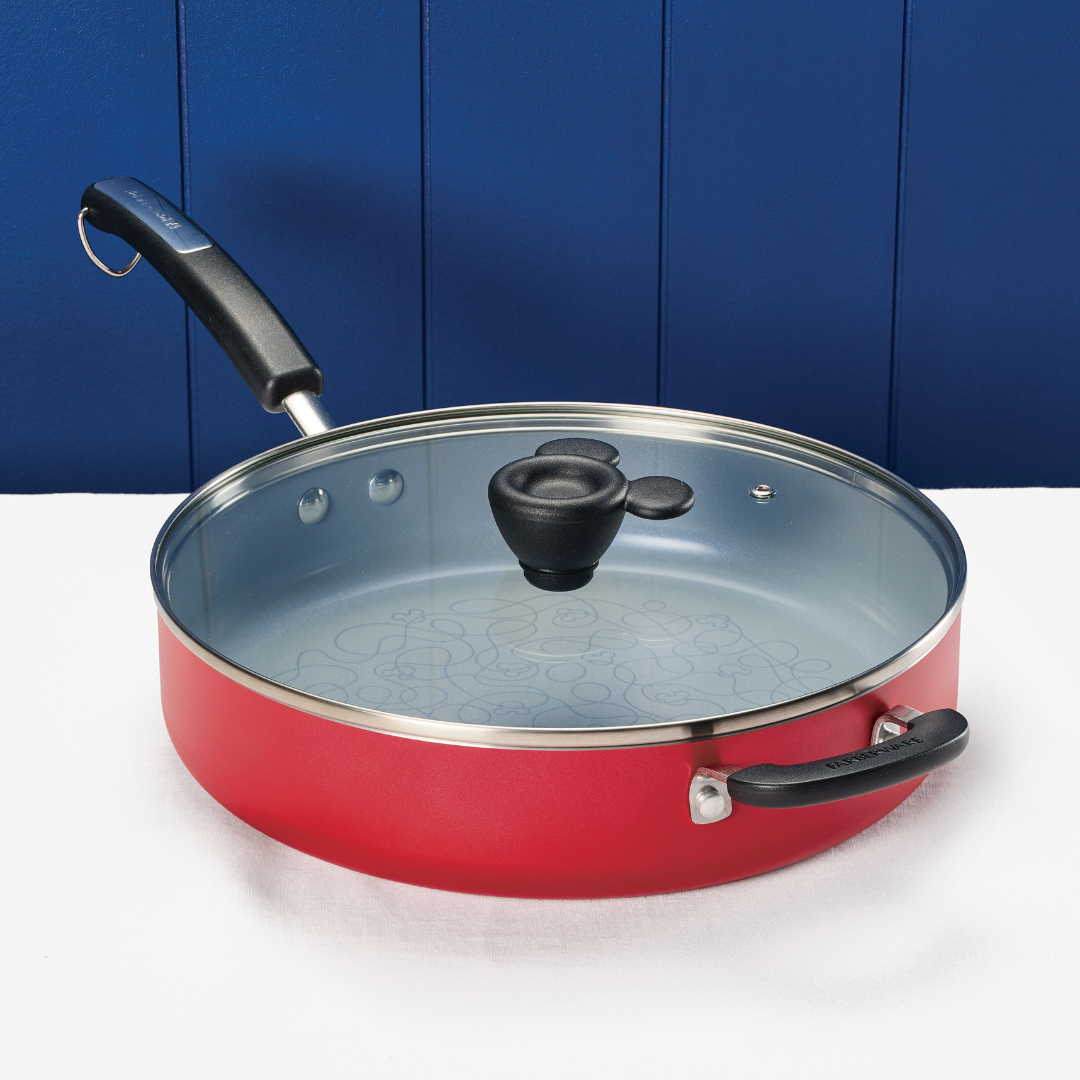 Red frying pan with a glass lid on a white surface against a blue background.