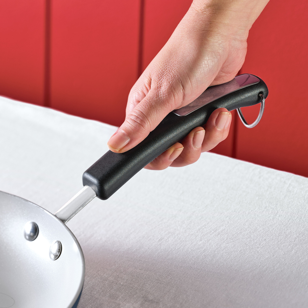 Hand holding the handle of a frying pan over a white surface.