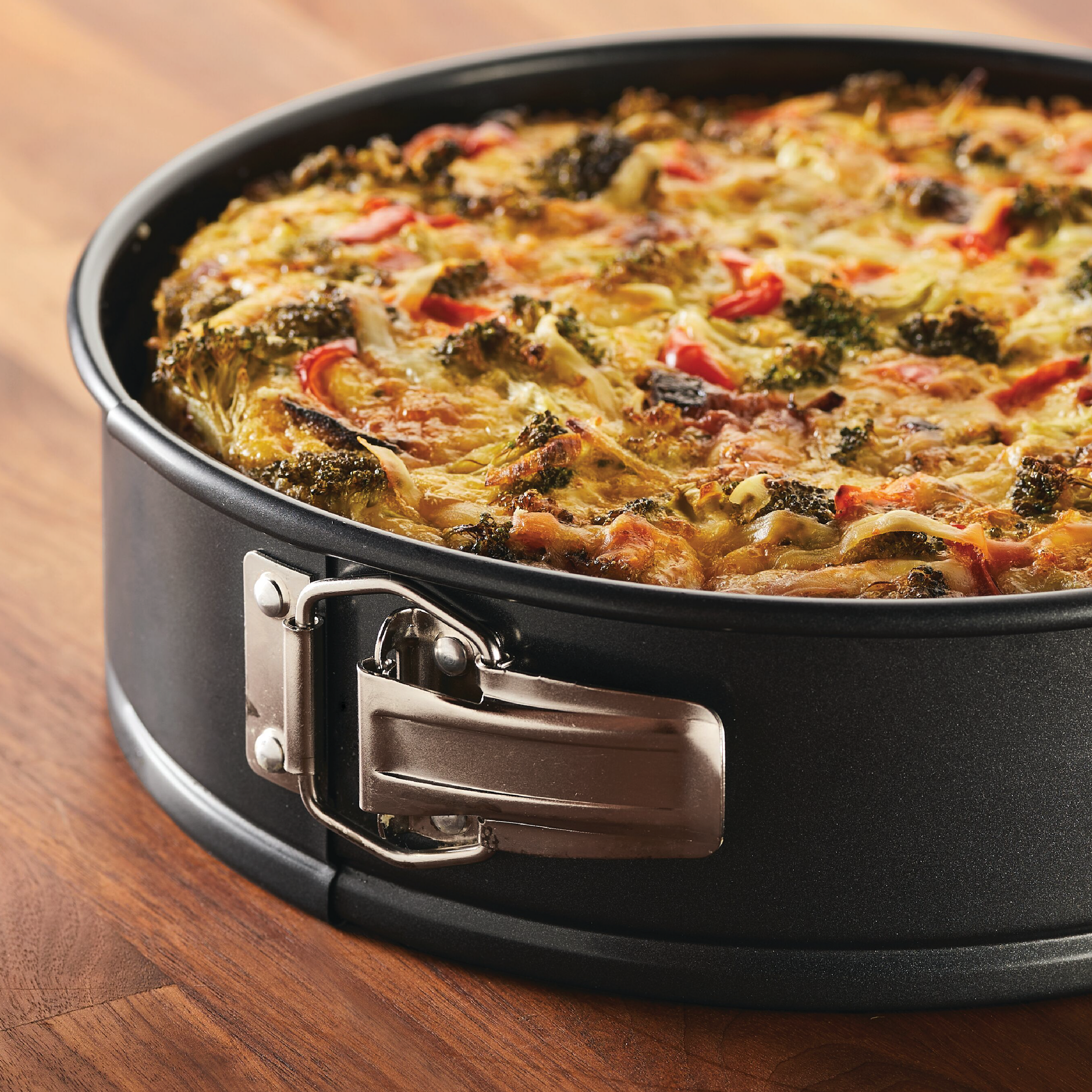 A vegetable quiche in a 9-inch nonstick round springform pan from the Bake with Mickey collection, resting elegantly on a wooden table.