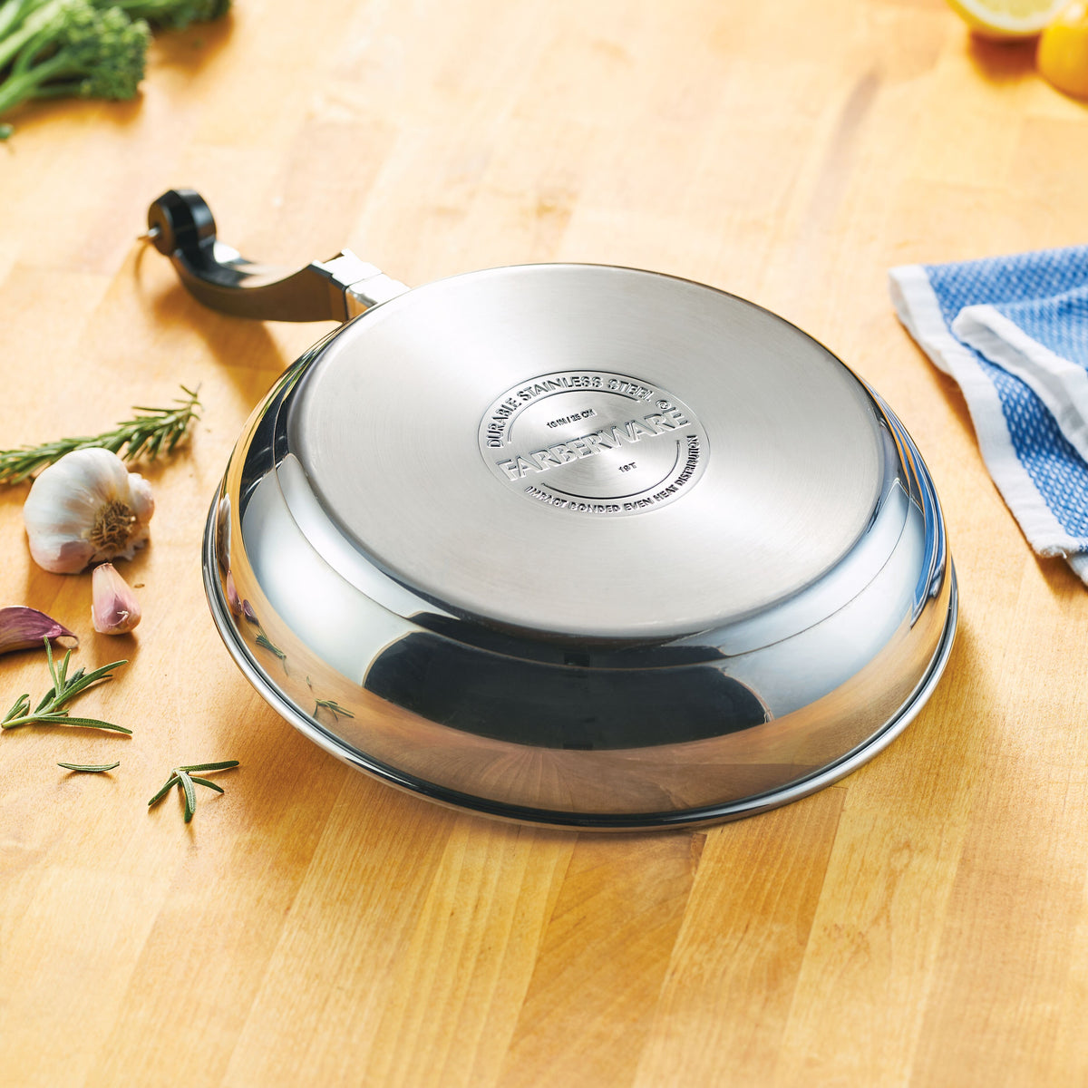 Stainless steel frying pan upside down on wooden countertop with herbs nearby.