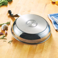 Stainless steel frying pan upside down on wooden countertop with herbs nearby.