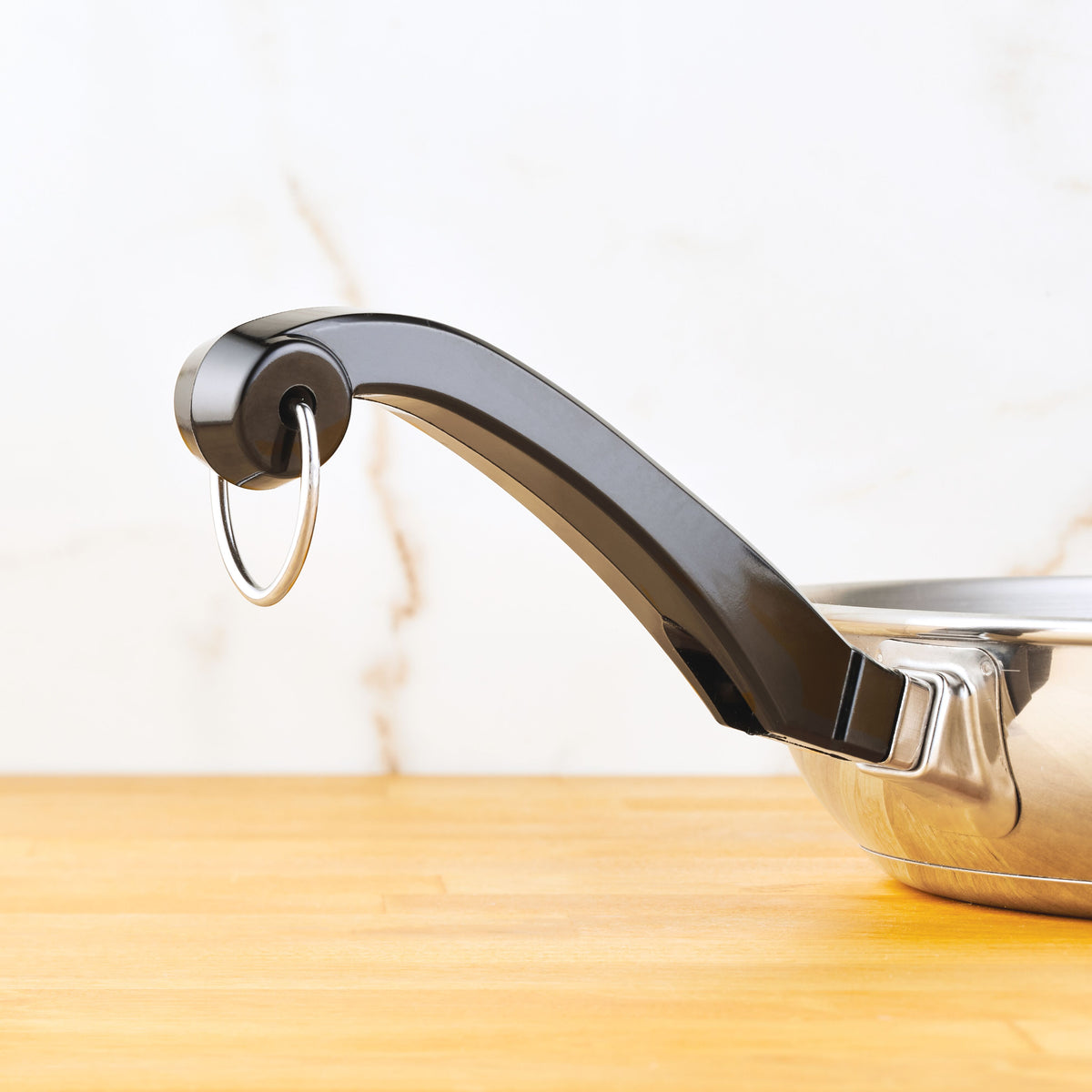 Close-up of a saucepan handle with a metal loop on a wooden surface.