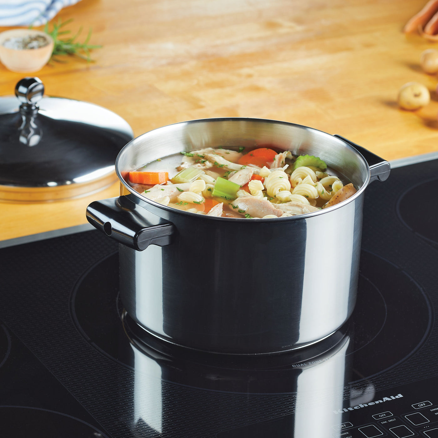 A Classic Series Stainless Steel 4-Qt. Saucepot simmers chicken noodle soup on the stovetop next to a lid, promising warmth and comfort. Ideal for pairing with mashed potatoes, this cookware remains dishwasher safe, ensuring an easy cleanup.