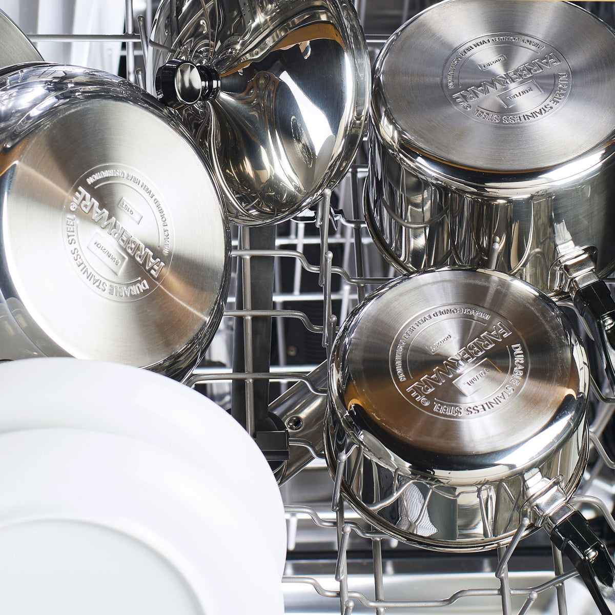Stainless steel cookware loaded in a dishwasher with a white plate.