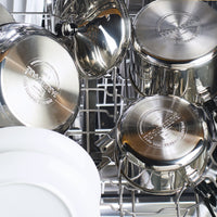 Stainless steel cookware loaded in a dishwasher with a white plate.
