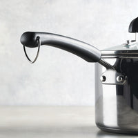 The 3-Quart Stainless Steel Saucepan by Farberware Brilliance, featuring a black handle and a matching lid, rests elegantly on a flat surface.