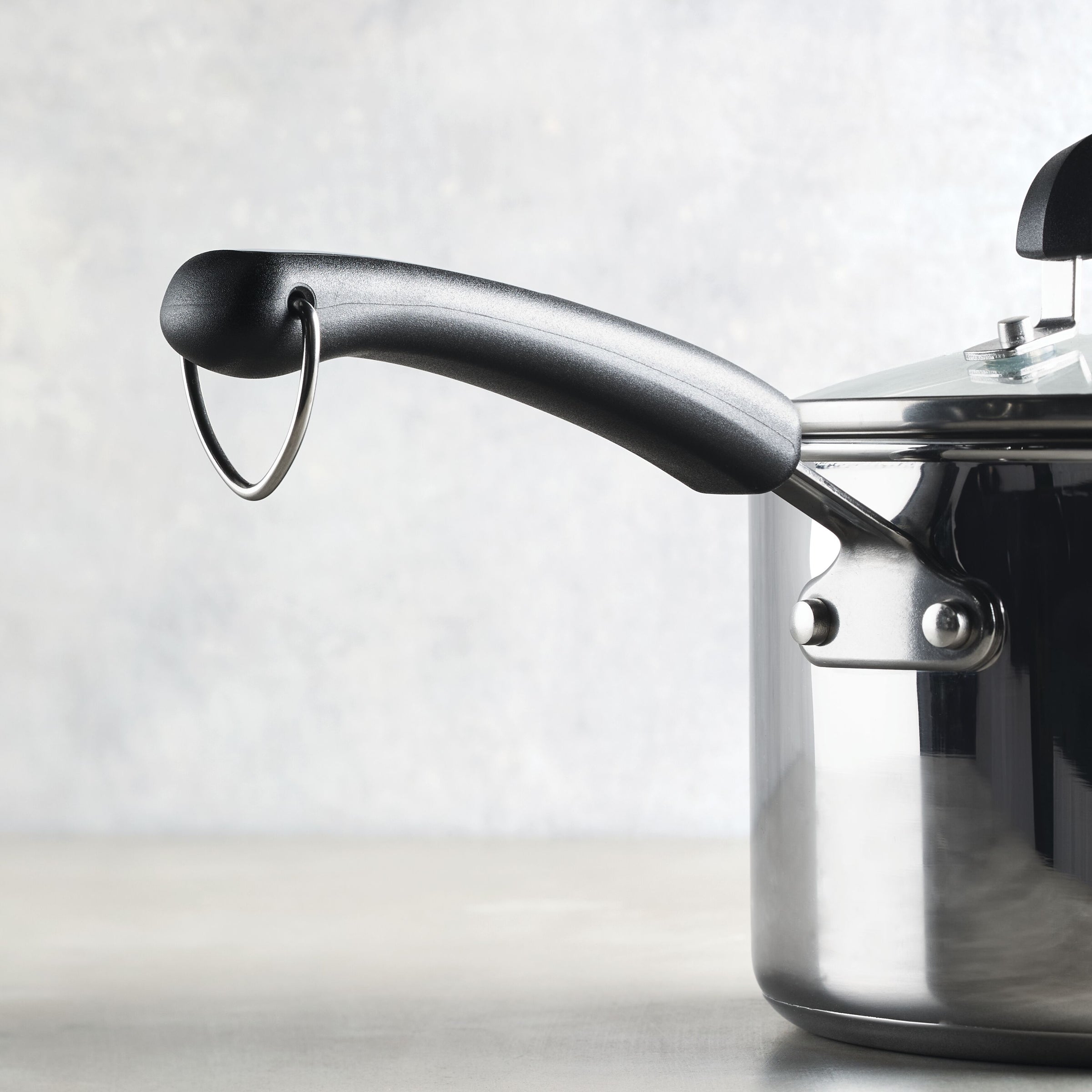 The 3-Quart Stainless Steel Saucepan by Farberware Brilliance, featuring a black handle and a matching lid, rests elegantly on a flat surface.