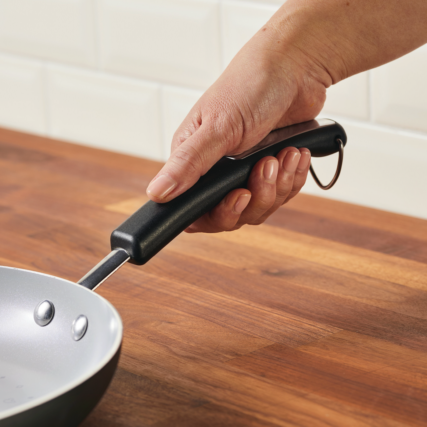 A hand grasps the handle of a frying pan from the 7-Piece Monochrome Ceramic Nonstick Cookware Set on a wooden countertop, highlighting its elegant ceramic nonstick interior.