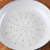 This white frying pan is part of the 7-Piece Monochrome Ceramic Nonstick Cookware Set, featuring a ceramic nonstick interior decorated with small gray shapes.