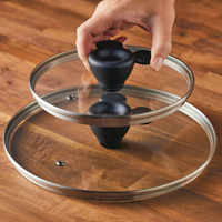 A hand holds a glass pot lid, its surface reflecting the warm tones of a wooden table, seamlessly fitting into the 7-Piece Monochrome Ceramic Nonstick Cookware Set.